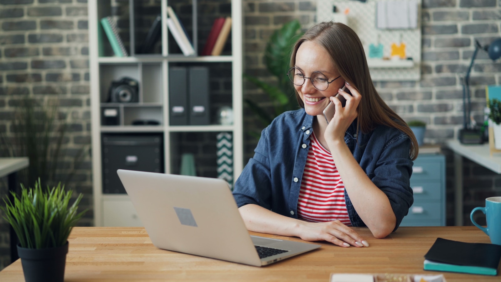 Scale your business with an AI phone answering service plan Business owner talking on a cell phone while working on a laptop, with an AI phone answering service handling incoming calls
